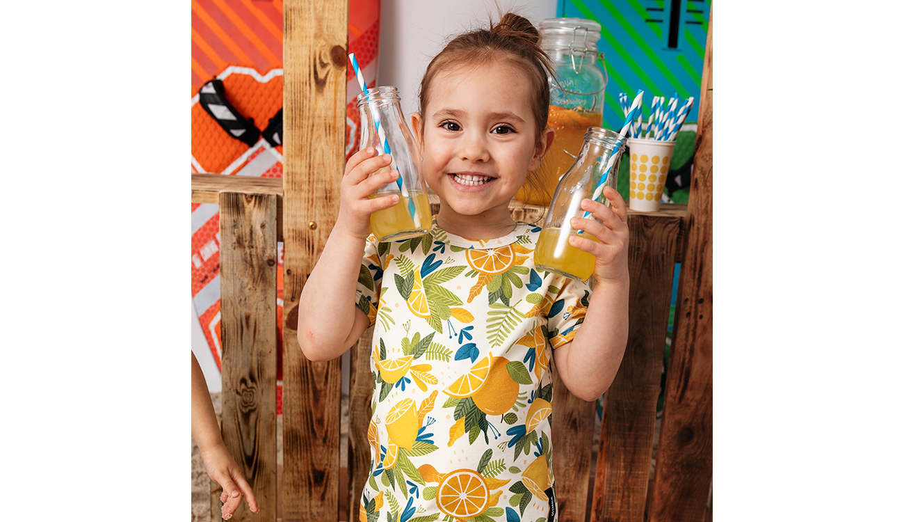 Uśmiechnięta dziewczynka z sokiem w rękach - sesja zdjęciowa ubrań marki Go Charlie - wzory Weroniki Wolskiej