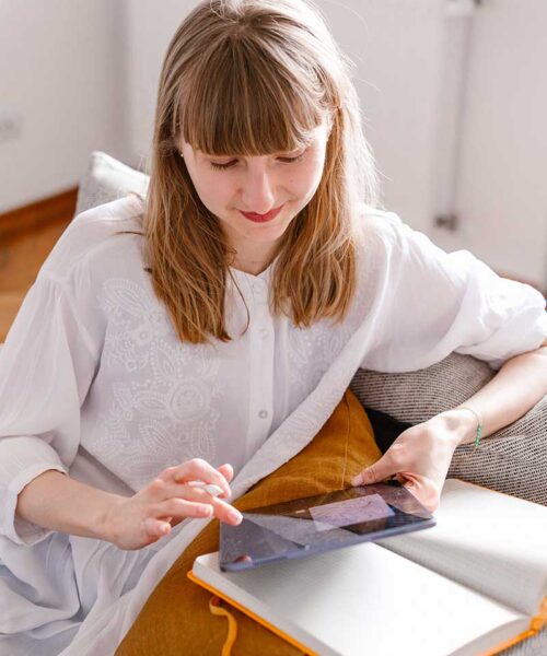 Dziewczyna, graficzka siedząca na kanapie z tabletem w rękach tworząca projekt graficzny.