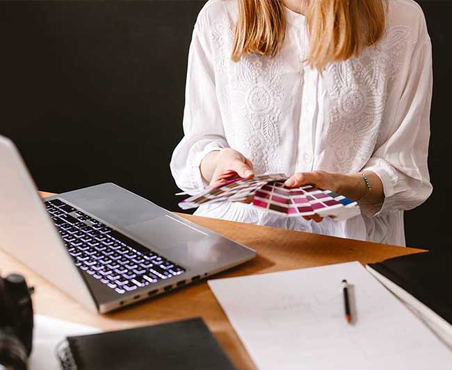 Dziewczyna, graficzka siedząca przy biurku, wybierająca kolor z próbników.