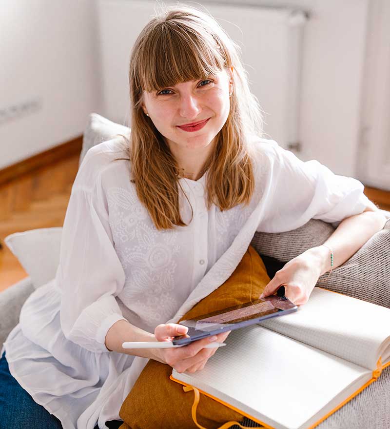 Dziewczyna, graficzka uśmiechnięta, siedząca na kanapie z tabletem w rękach.