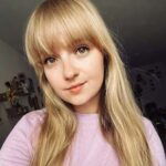 Martyna Ruszkowska — opinia o Kursie Projektowania Graficznego w Akademii Projektowania Weroniki Wolskiej; młoda kobieta z długimi blond włosami i grzywką, w jasnofioletowej bluzce, uśmiecha się delikatnie do aparatu w domowym wnętrzu.