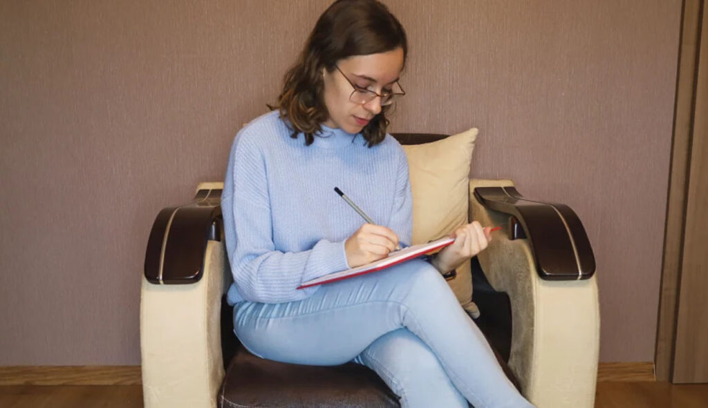 Magdalena Kita – uczestniczka Kursu Projektowania Graficznego w Akademii Projektowania stworzonego przez Weronikę Wolską – podczas pracy nad projektem zaliczeniowym, siedząca w fotelu z notatnikiem. Kurs obejmuje grafikę komputerową, design, reklamę i marketing wizualny. Początki w branży kreatywnej - wywiad.