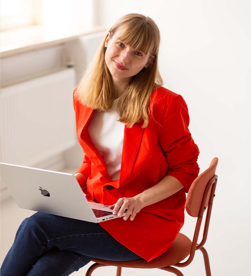 Uśmiechnięta edukatorka Weronika Wolska z laptopem w czerwonej marynarce – darmowe szkolenie z projektowania graficznego, Akademia Projektowania. Artykuł blogowy Weronika Wolska. Grafika, design, edukacja, kursy, Kurs Projektowania Graficznego w Akademii Projektowania, szkolenia.