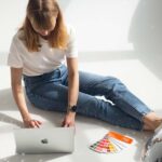 Weronika Wolska pracująca przy laptopie z próbnikiem kolorów i kulami dyskotekowymi – kreatywna praca z narzędziami AI w projektowaniu graficznym. Artykuł blogowy Weronika Wolska. Grafika, design, edukacja, kursy, Kurs Projektowania Graficznego w Akademii Projektowania, szkolenia.