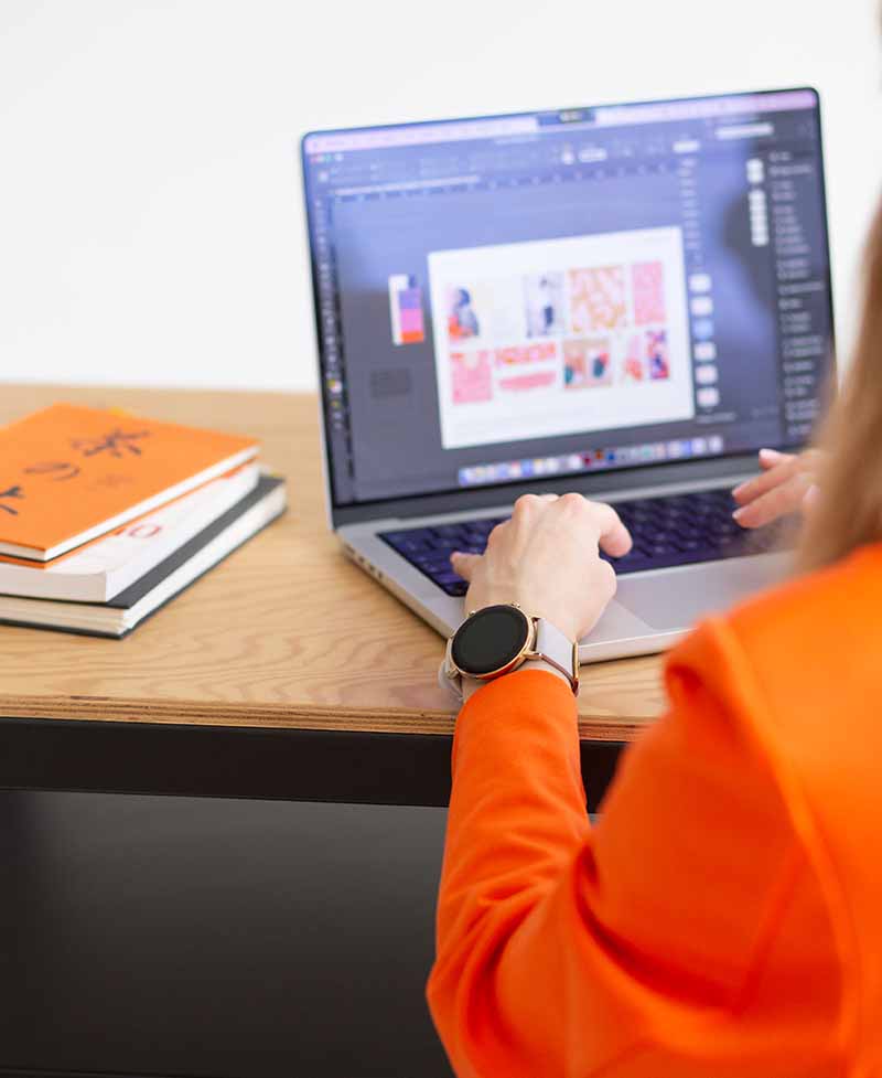 Weronika Wolska – twórczyni Akademii Projektowania – pracuje przy laptopie nad projektami graficznymi w programie do edycji. W tle widoczne są szkicowniki i książki o designie. Zdjęcie ilustruje artykuł blogowy z wywiadem z Aleksandrą Chlebowską – absolwentką Kursu Projektowania Graficznego, która dzieli się swoją ścieżką nauki grafiki komputerowej, budowy portfolio i pracy w branży kreatywnej jako początkująca freelancerka.