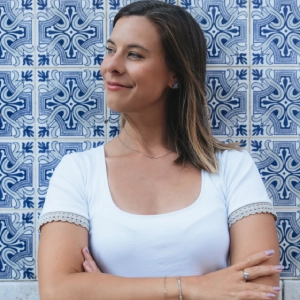 Klaudia Pawelec – absolwentka Kursu Projektowania Graficznego w Akademii Projektowania Weroniki Wolskiej – stoi z uśmiechem na tle ozdobnej ściany z niebiesko-białych kafli, symbolizując pewność siebie i kreatywność zdobytą w trakcie nauki grafiki komputerowej, designu i projektowania wizualnego jako freelancerka w branży kreatywnej.