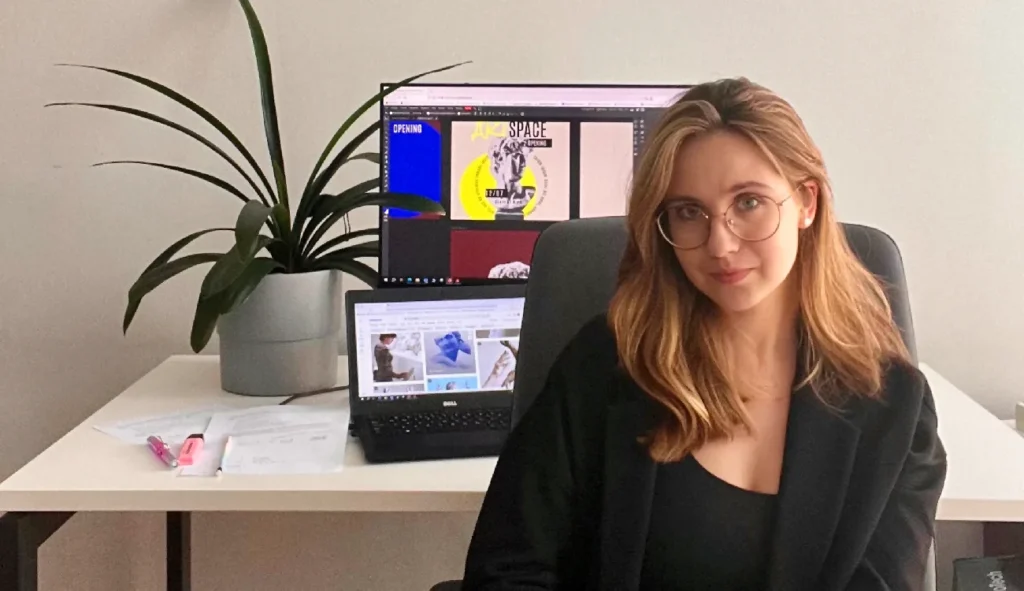 Aleksandra Chlebowska – absolwentka Kursu Projektowania Graficznego Weroniki Wolskiej – siedzi przy biurku z komputerem i monitorami, pracując nad projektami graficznymi w ramach nauki designu i budowy portfolio w Akademii Projektowania. Zdjęcie przedstawia młodą graficzkę rozwijającą swoje umiejętności z zakresu grafiki komputerowej i freelancingu.