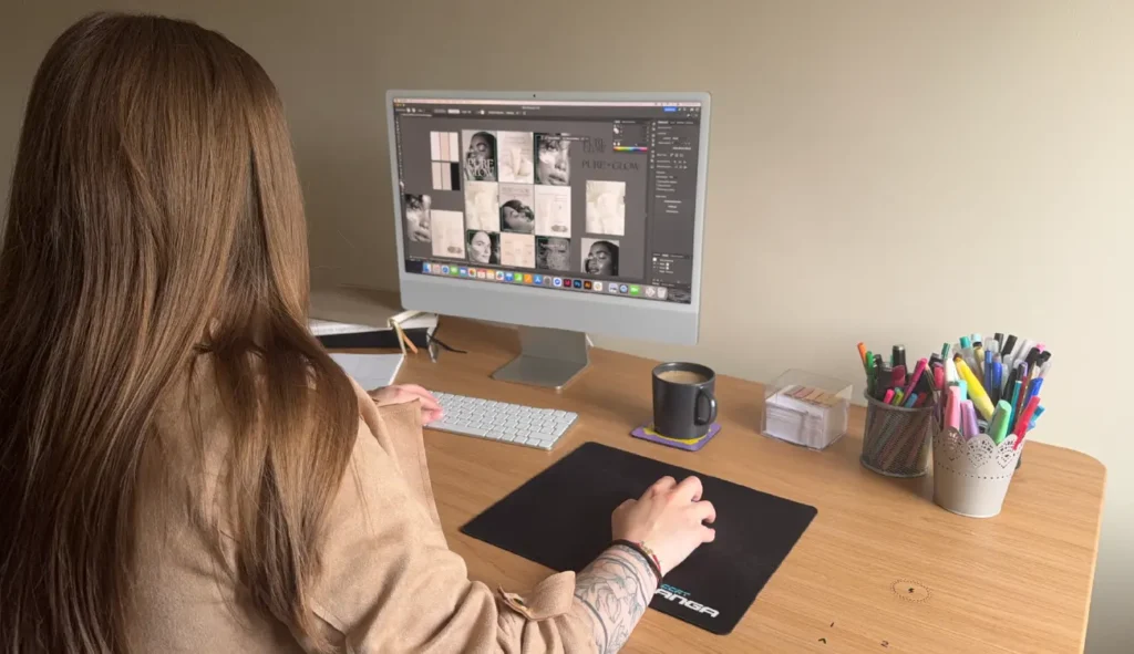 Oliwia Nowicka – absolwentka Kursu Projektowania Graficznego w Akademii Projektowania Weroniki Wolskiej – przy biurku, pracująca nad projektem graficznym w programie komputerowym. Na ekranie widoczna identyfikacja wizualna marki Pure Glow. Otoczenie kreatywne: notesy, kubek z kawą, długopisy i markery. Przykład pracy freelancera w branży grafiki komputerowej i designu.